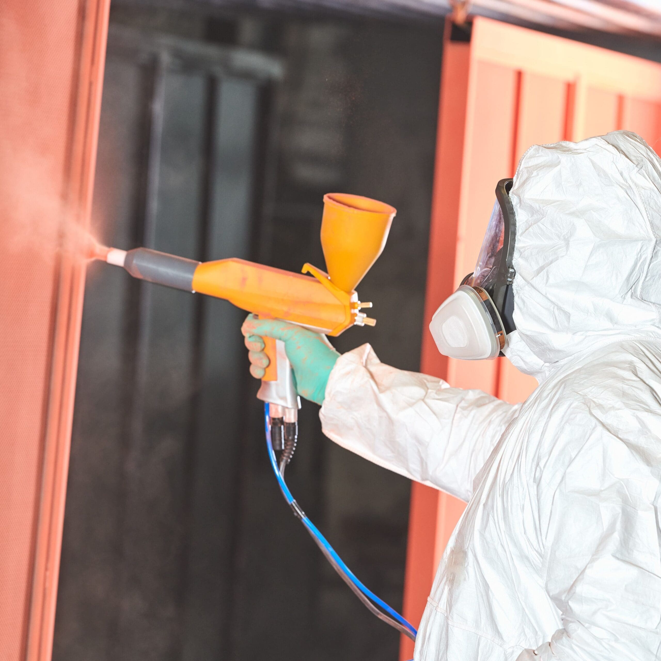 A powder-coating specialist applies an orange coating to a large metal door in production