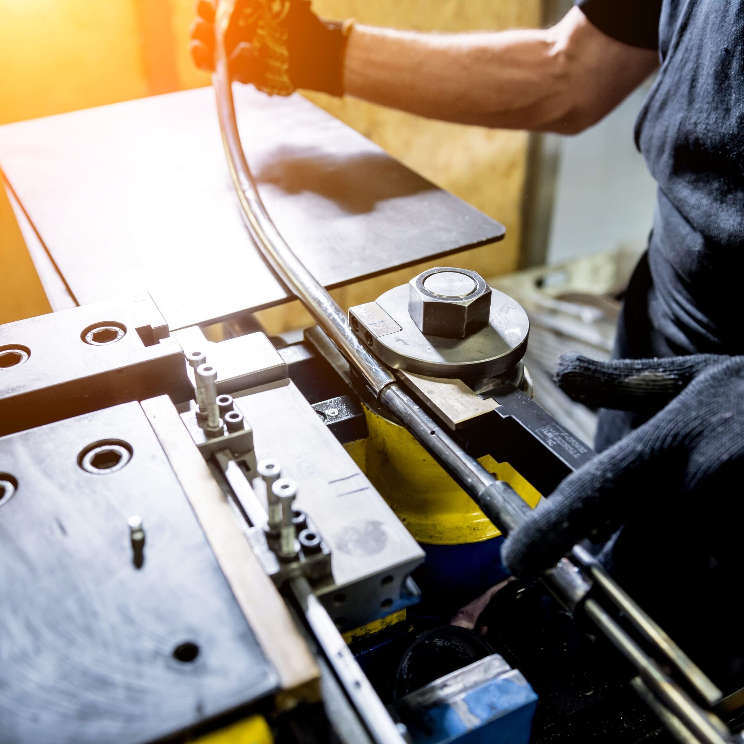 A metalworker bends a length of steel pipe using a pipe-bending machine