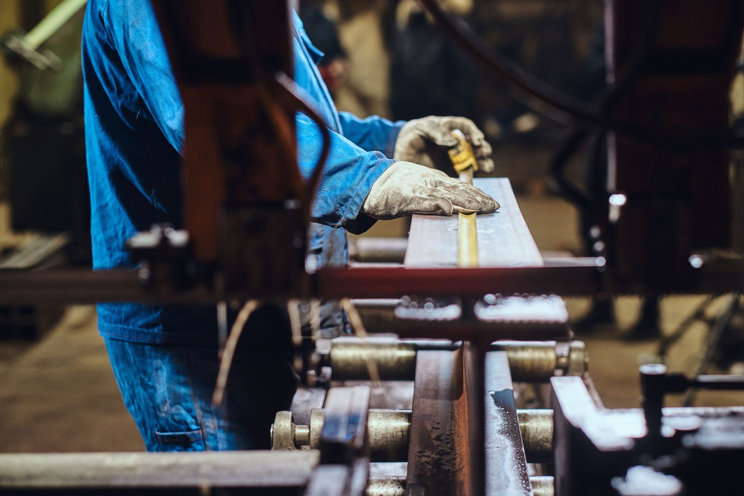 Metal fabrication worker taking precise measurements on steel rail components in a custom fabrication facility